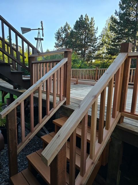 Wooden accessibility ramp with handrails beside a house deck, surrounded by trees and stairs.