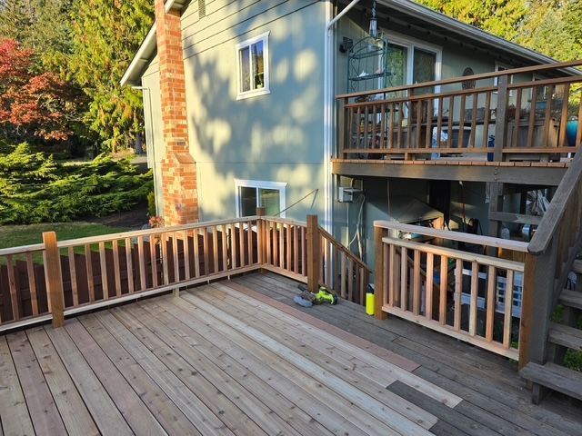 Wooden backyard deck beside a house with railings and stairs, in warm sunlight.