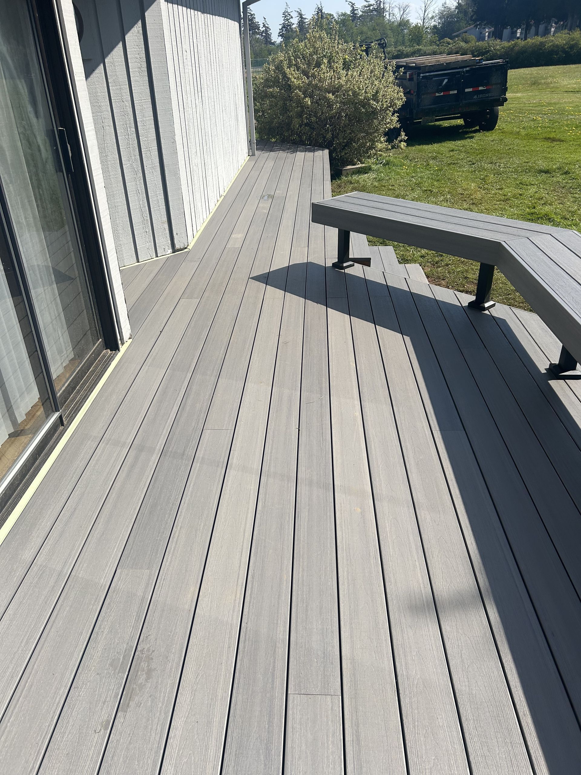 Deck beside house with bench, gray boards, and sunlight casting long shadows.