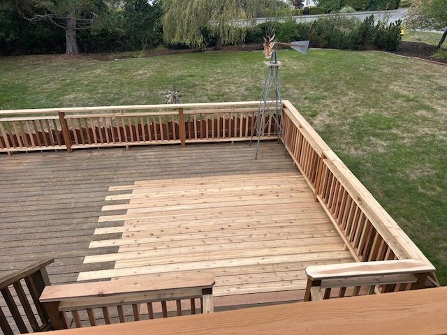 Backyard wooden deck with railings and steps, overlooking a grassy yard and garden.