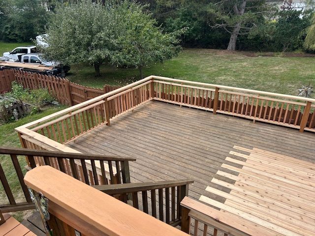 Wooden deck with railings and steps overlooking a grassy yard and parked cars