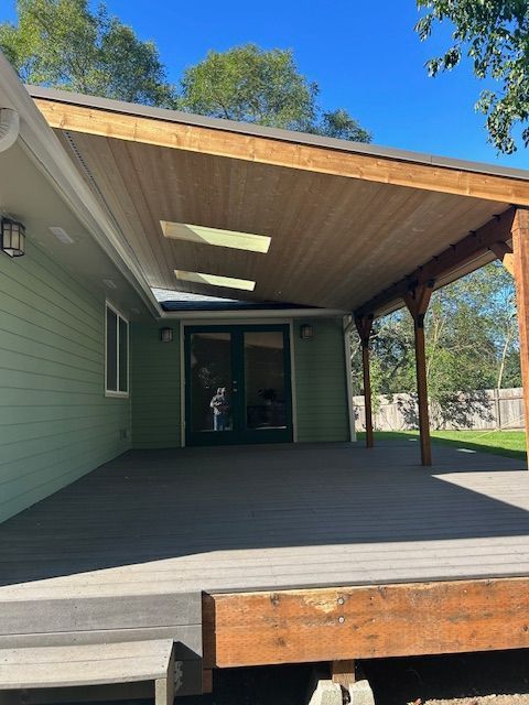 Covered wooden porch with green siding and skylights, opening to a glass doorway
