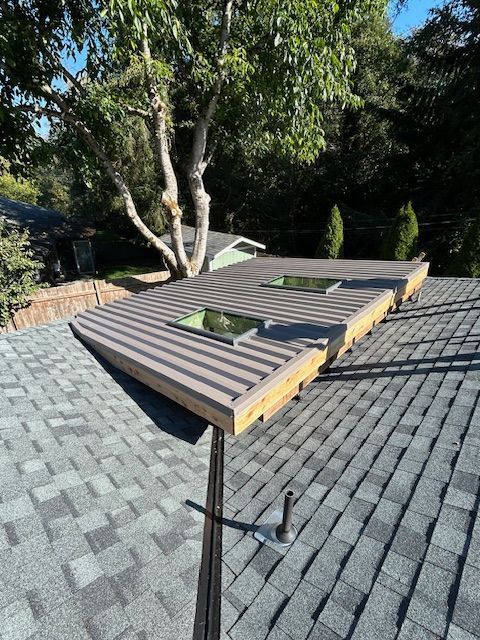 Wooden rooftop frame on gray shingles with trees in the background