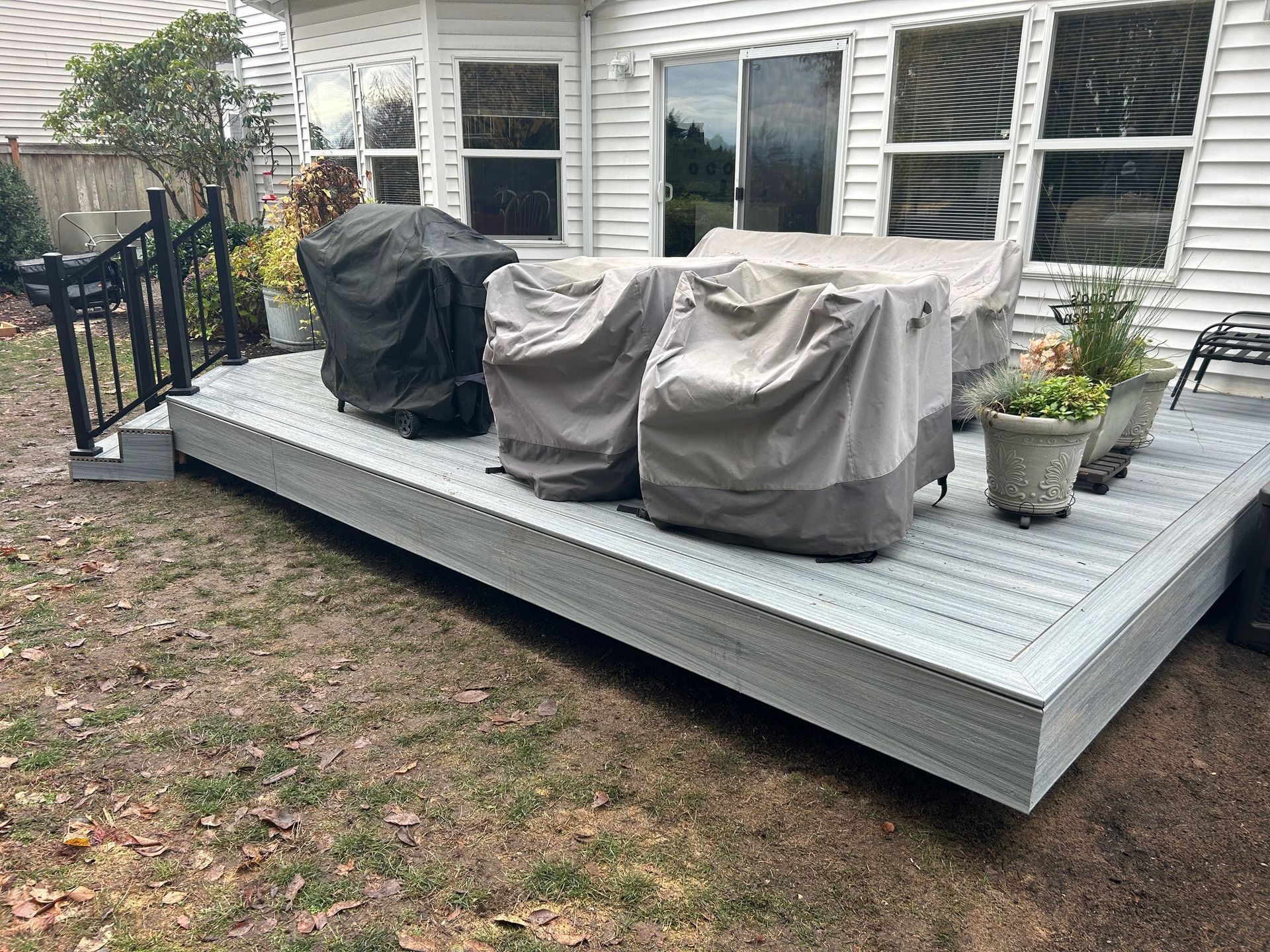 Back patio with covered grill, covered seating, and potted plants by the house