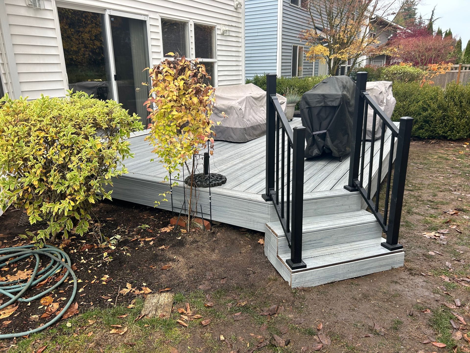 Back deck with black railings, steps, and covered patio furniture beside a house and autumn shrubs