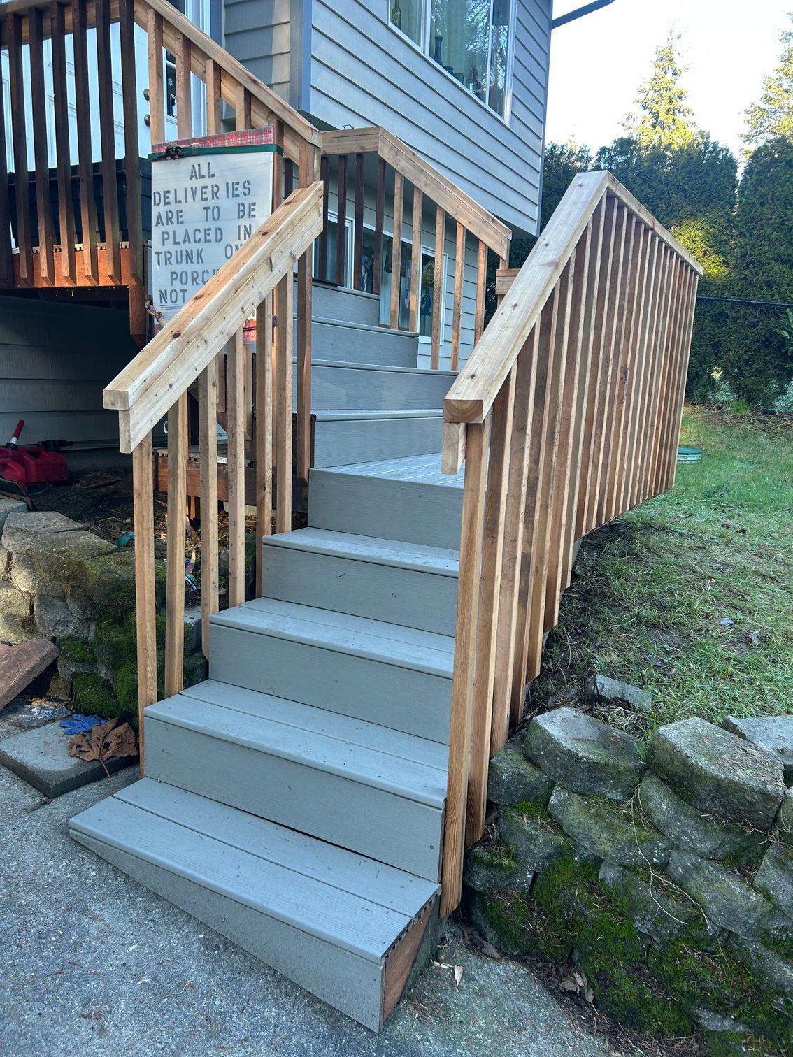 Outdoor wooden staircase with gray steps and railings leading up to a house porch.