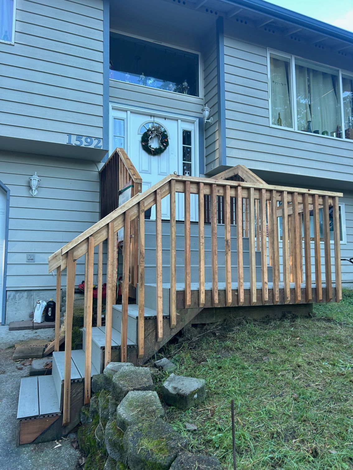 Wooden accessibility ramp leading to a front door on a blue house, with steps and a small porch.