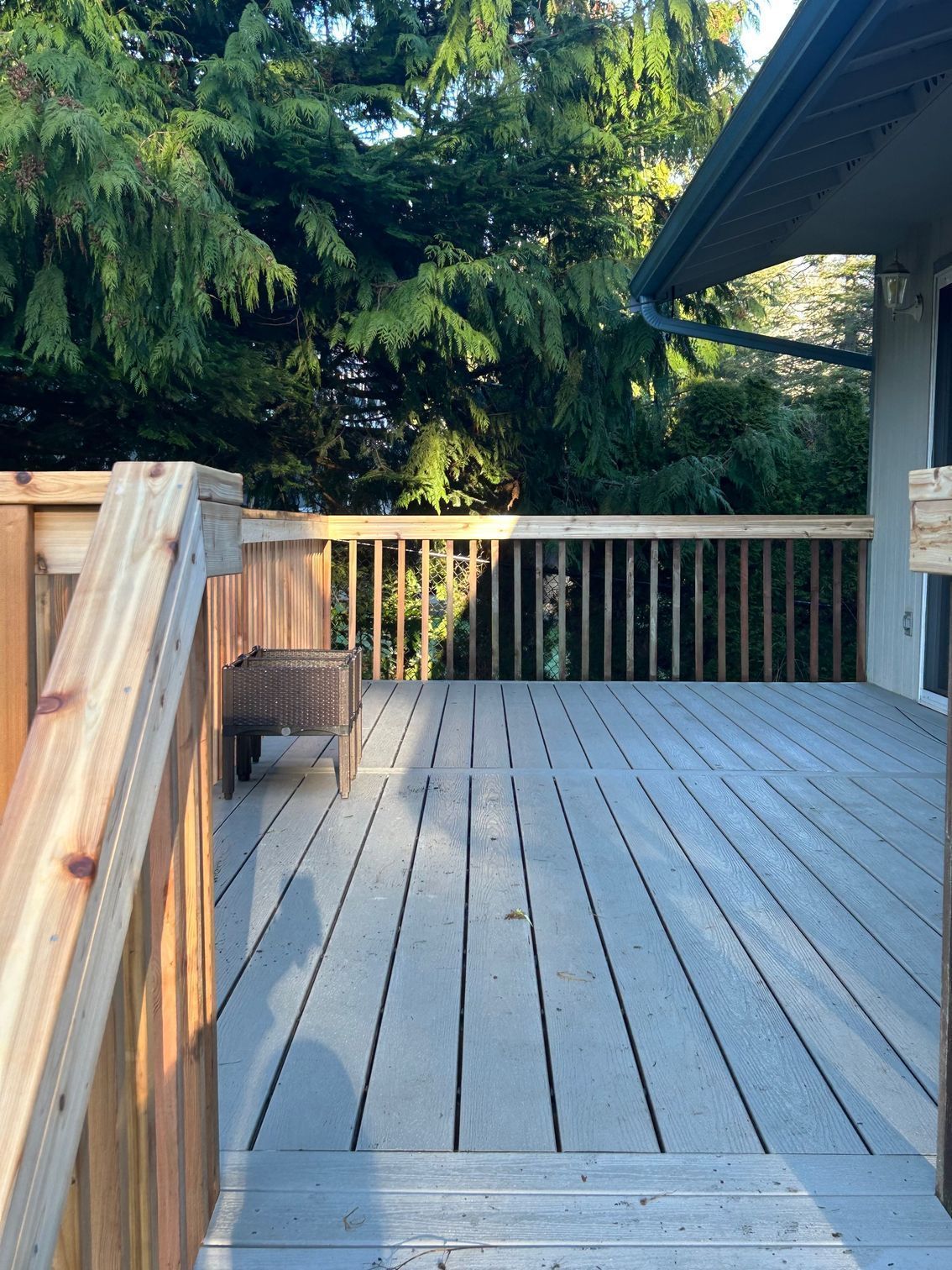 Wooden deck with railings and steps, overlooking green trees beside a house.