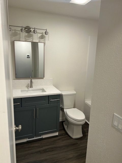 Small bathroom with dark vanity, mirror, white toilet, and wood-look floor.