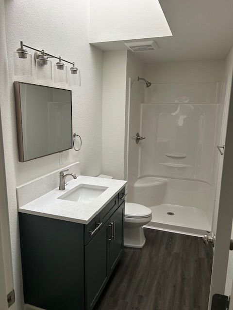 Modern bathroom with black vanity, white sink, mirror, toilet, and walk-in shower