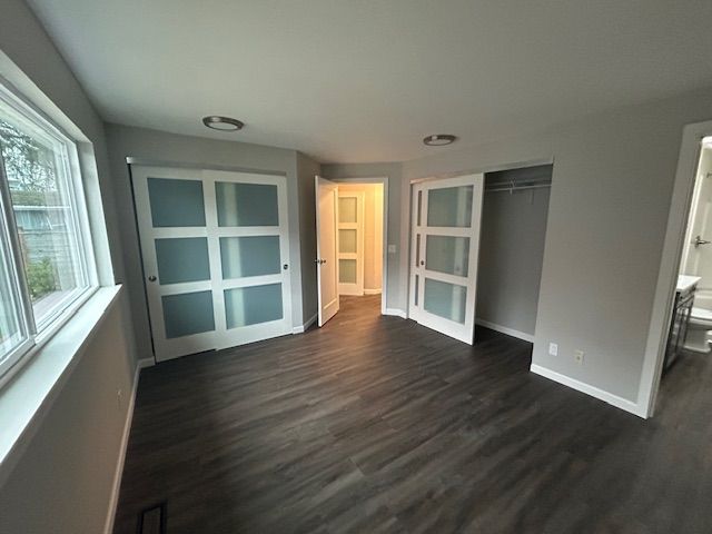 Empty modern room with dark wood floors, gray walls, white-framed French doors, and a window bench.