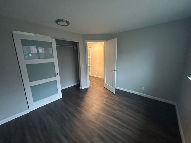 Empty modern room with dark wood floors, gray walls, and an open door to a lit hallway.
