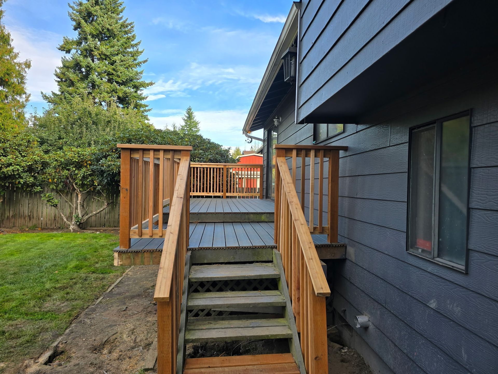 Backyard wooden stairs with railings beside a dark gray house and fenced lawn