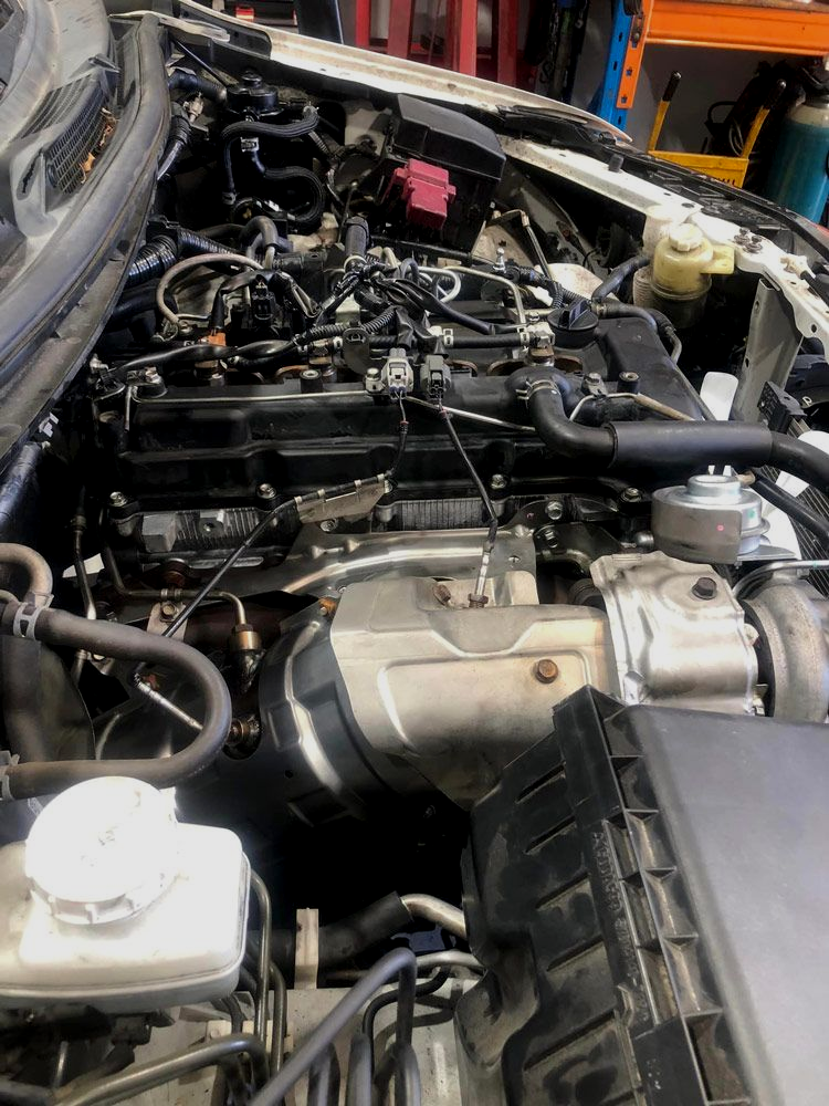 Car engine bay with various components visible, in a repair shop setting. — Experienced Mechanics on the Gold Coast