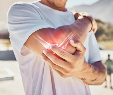 Photograph of a white male, unspecified age in a white T-shirt holding his elbow. 