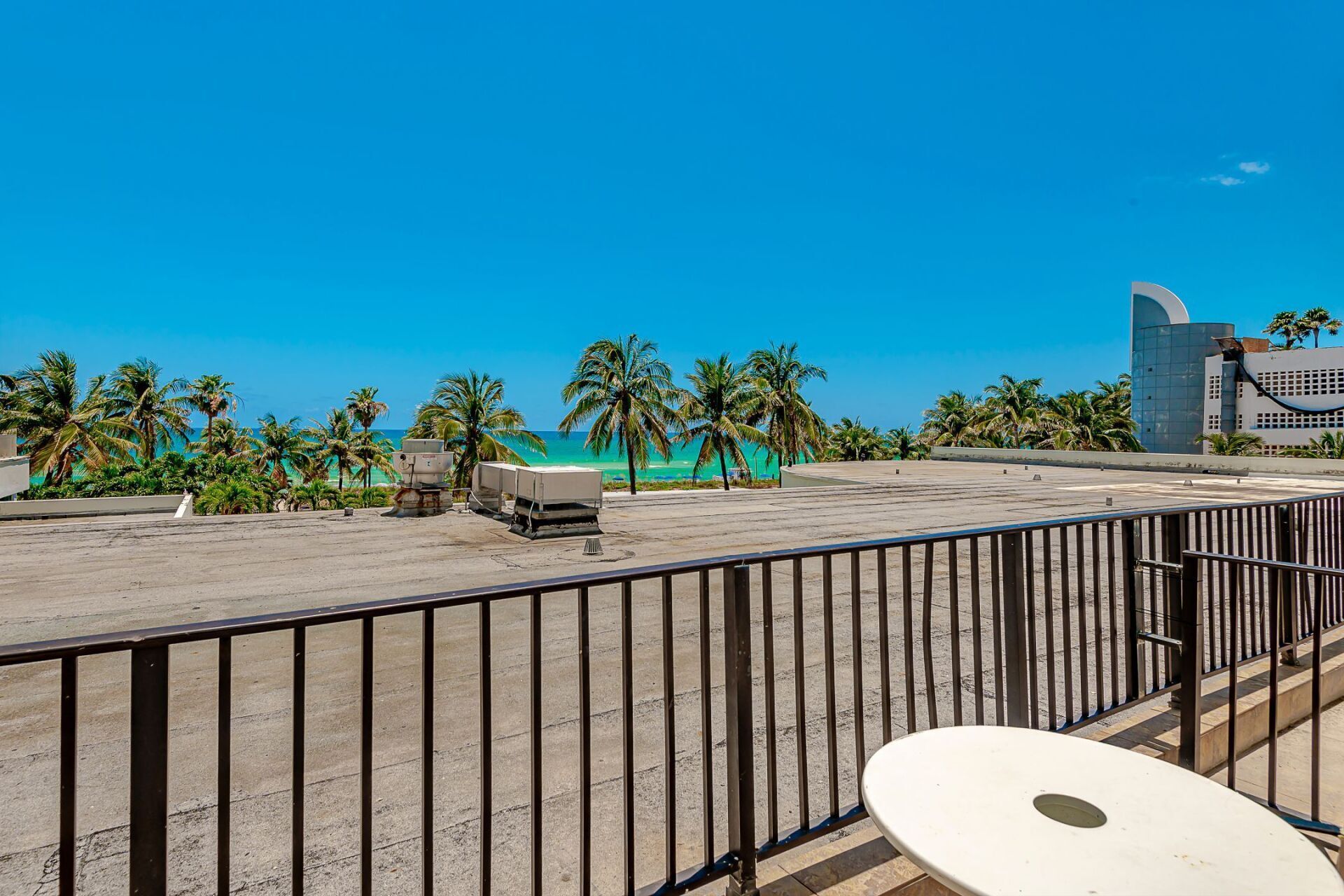 A view of the beach from a balcony with a table and chairs.