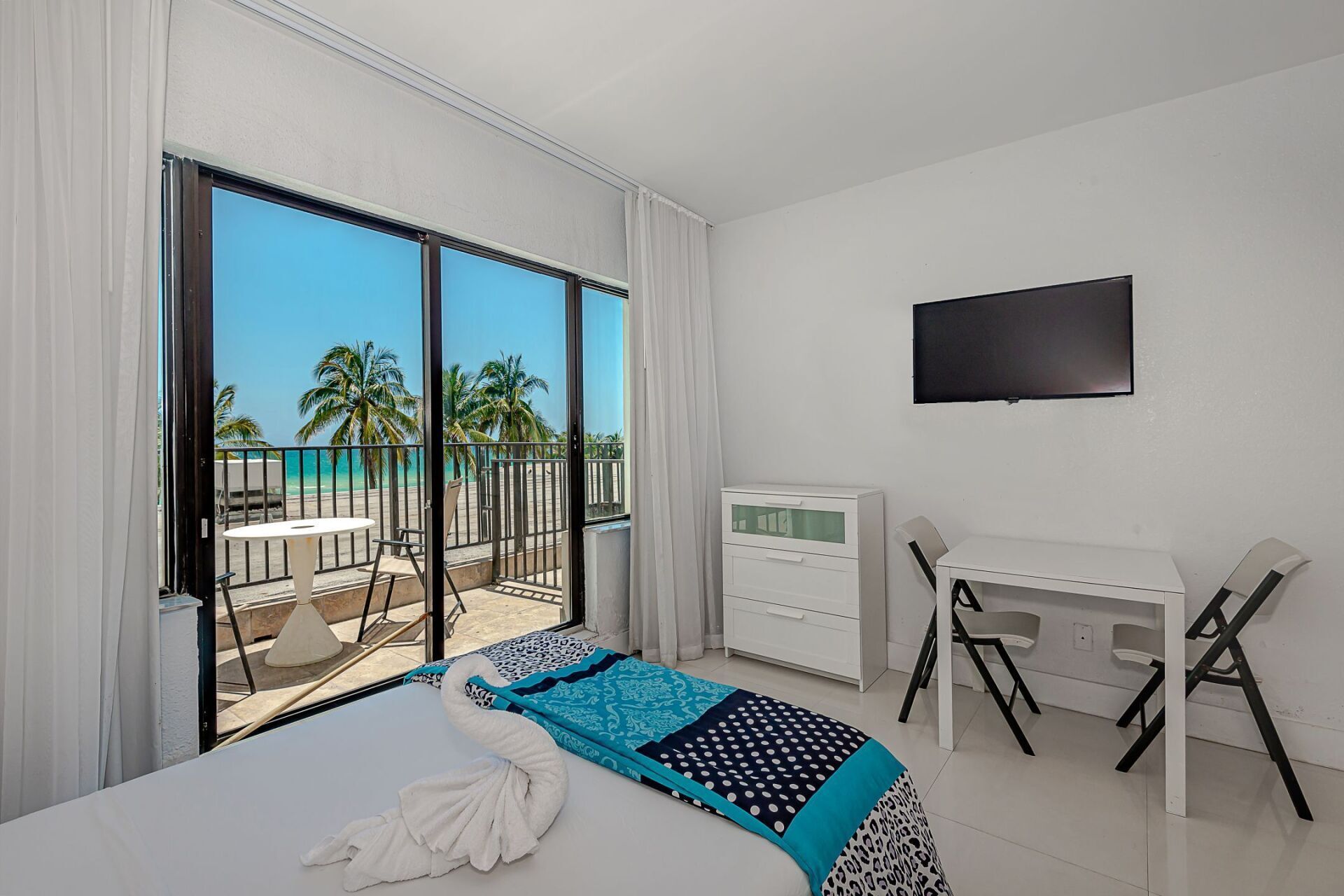 A hotel room with a bed , desk , television and balcony.