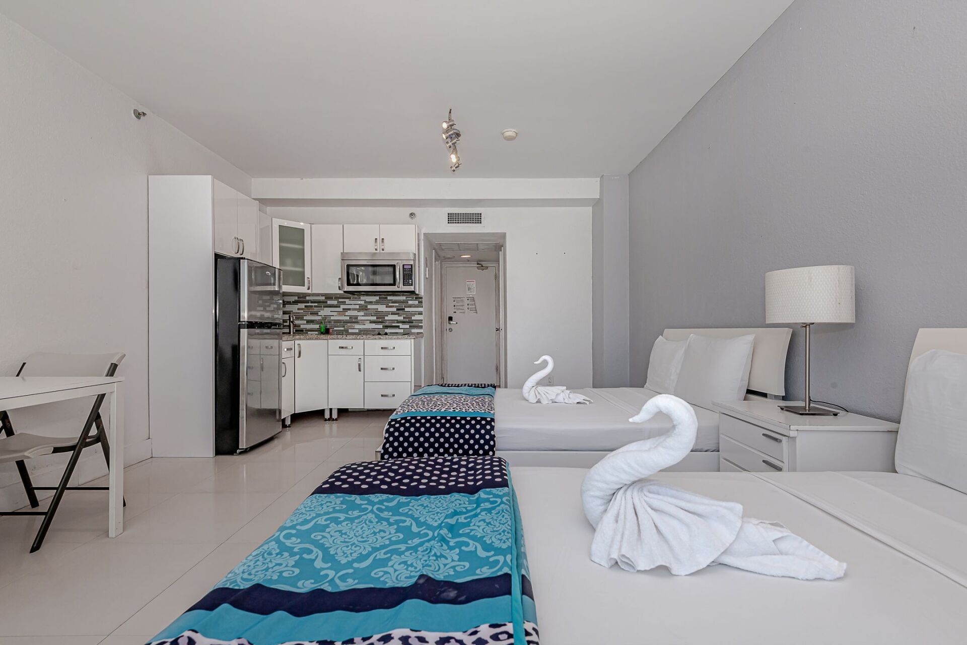 A hotel room with two beds , a kitchen and a swan made out of towels.