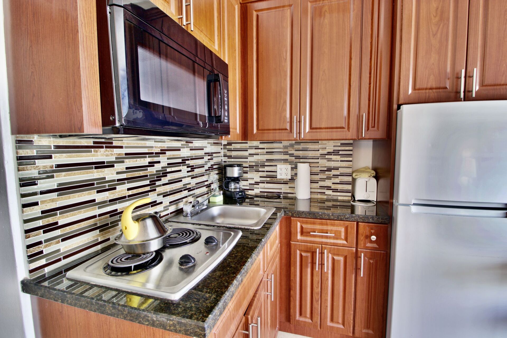 A kitchen with a stove top oven , microwave , refrigerator and sink.