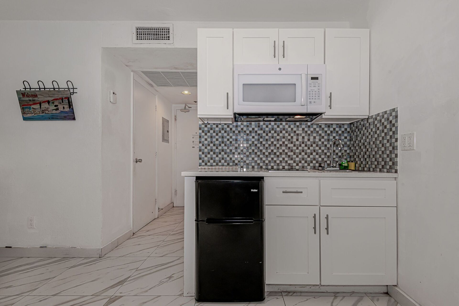 A kitchen with white cabinets , a black refrigerator , a microwave , and a sink.