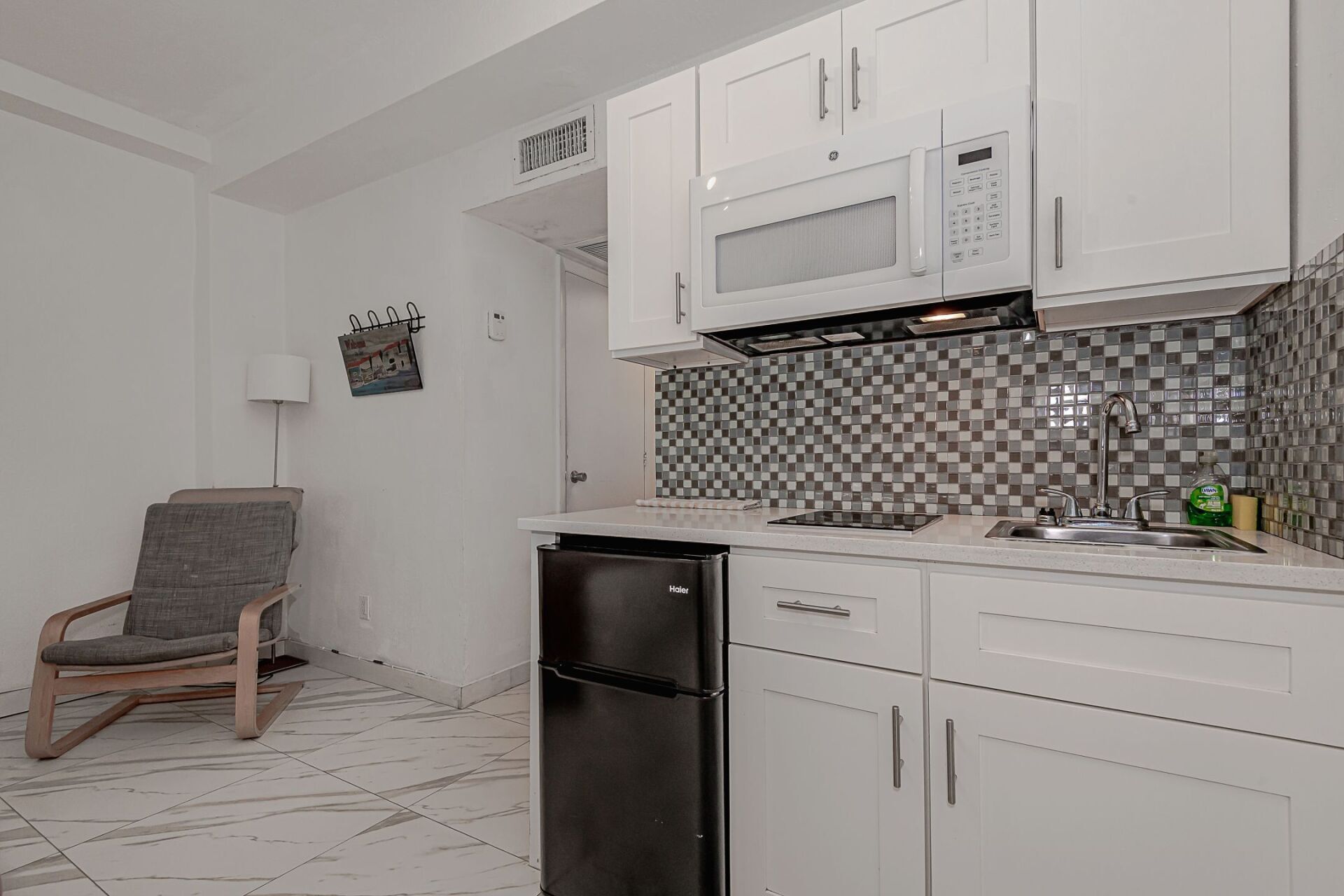 A kitchen with white cabinets , a black refrigerator , a microwave , and a chair.