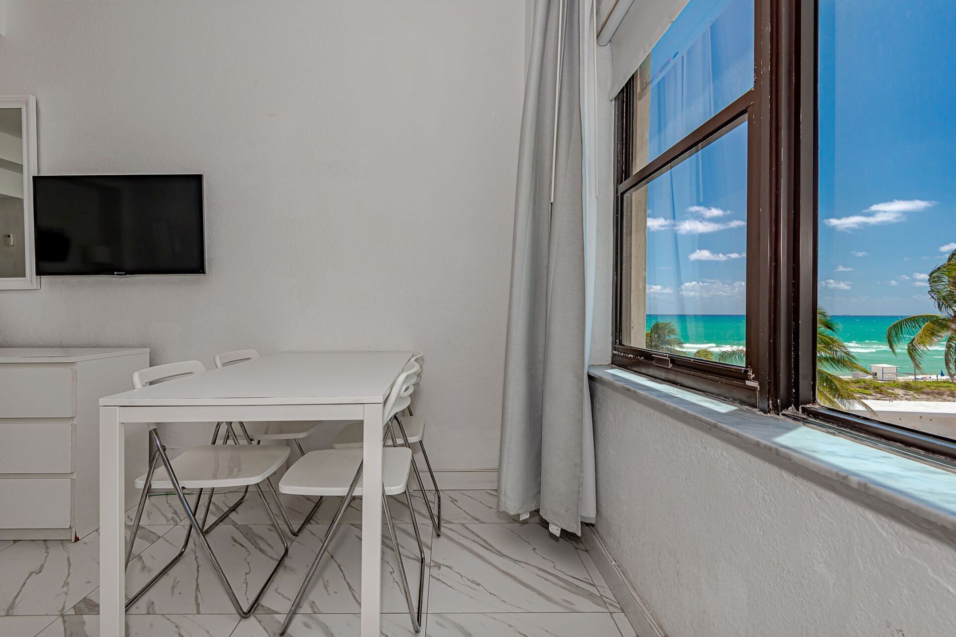 There is a table and chairs in the room with a view of the ocean.