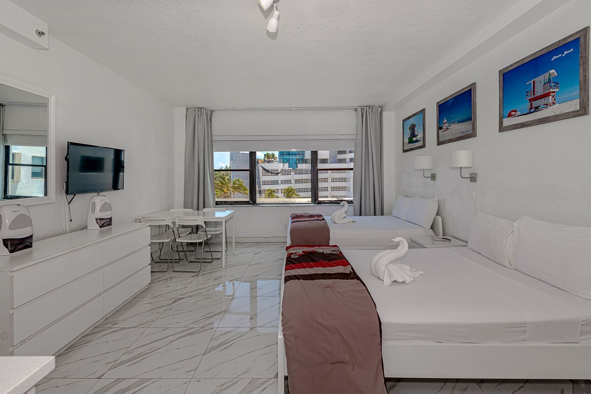 A hotel room with two beds , a dresser , a television and a table.