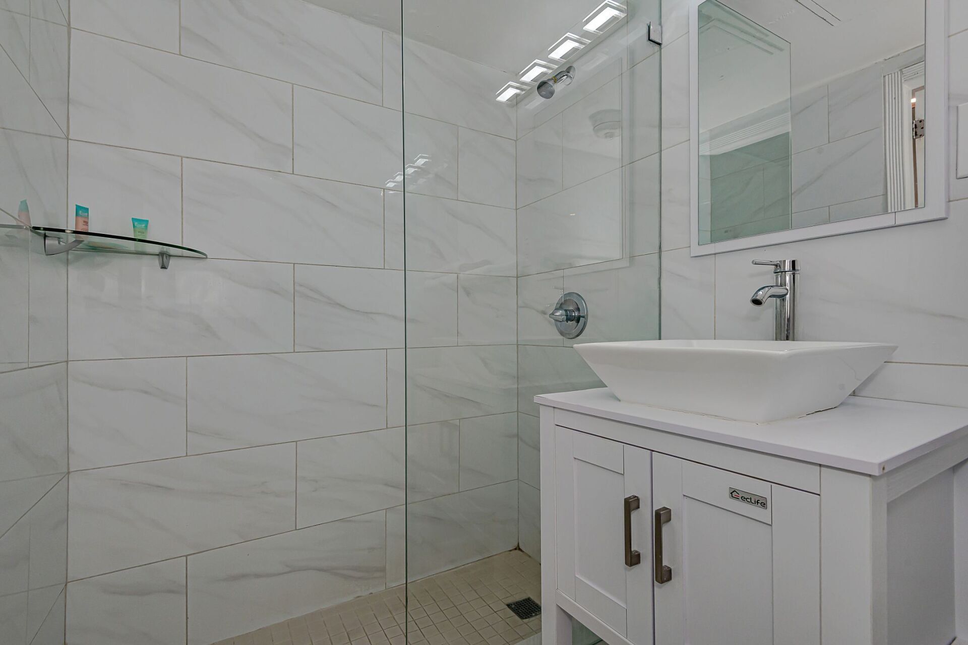 A bathroom with a sink , mirror and walk in shower.