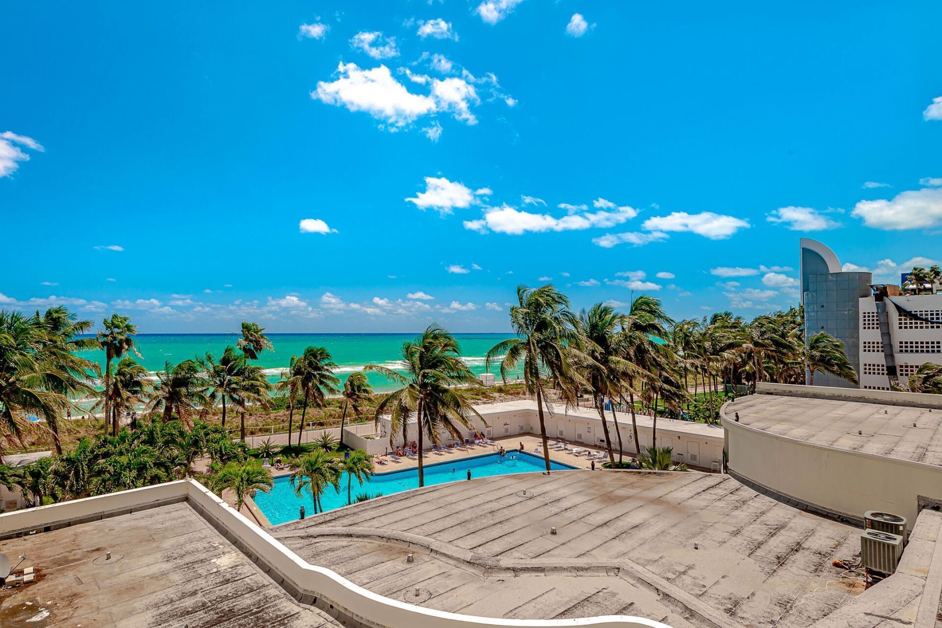 A view of a swimming pool and the ocean from the roof of a building.