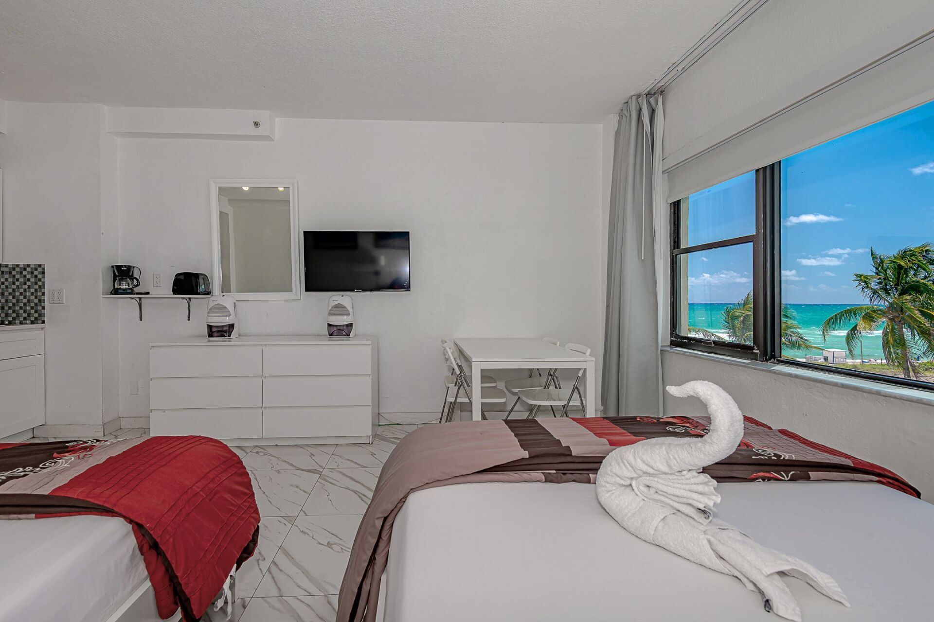 A hotel room with two beds , a dresser , a television and a view of the ocean.