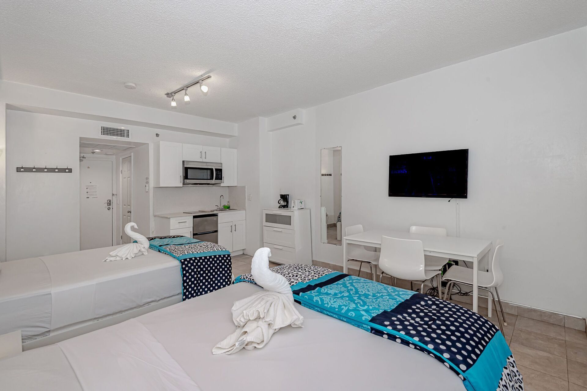 A hotel room with two beds , a table , chairs and a flat screen tv.