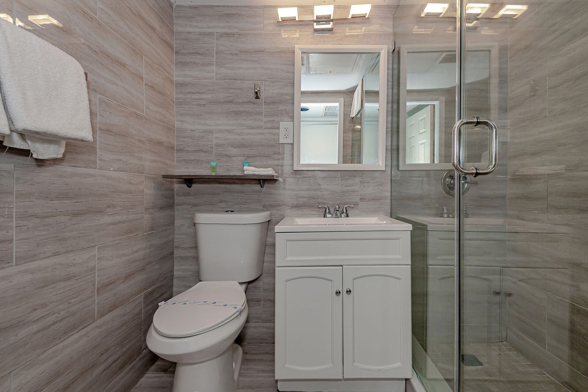 A bathroom with a toilet , sink , mirror and walk in shower.