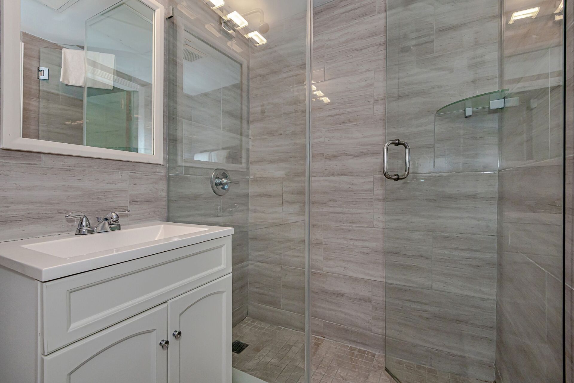 A bathroom with a sink , mirror and walk in shower.