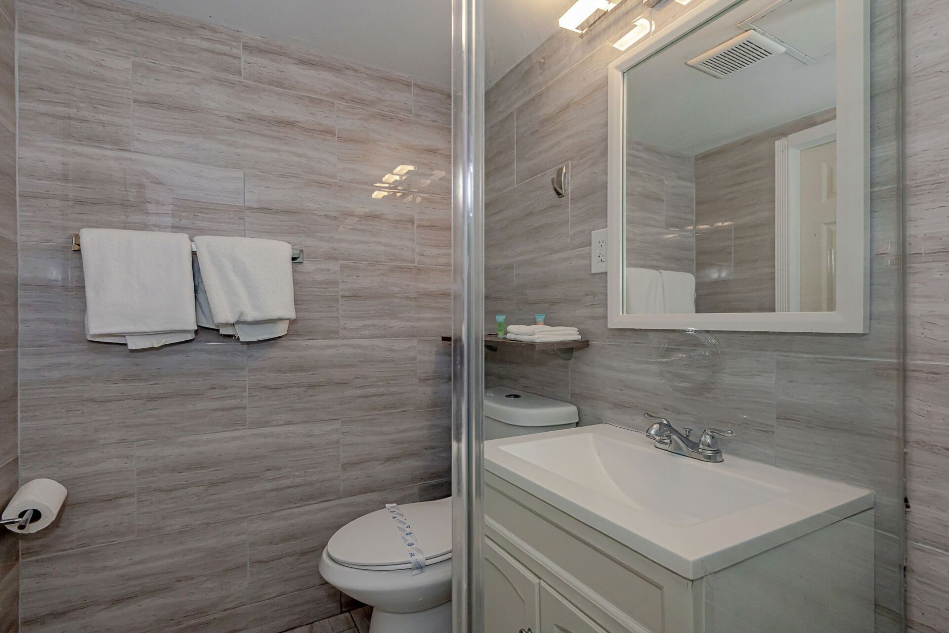 A bathroom with a toilet , sink , mirror and shower.