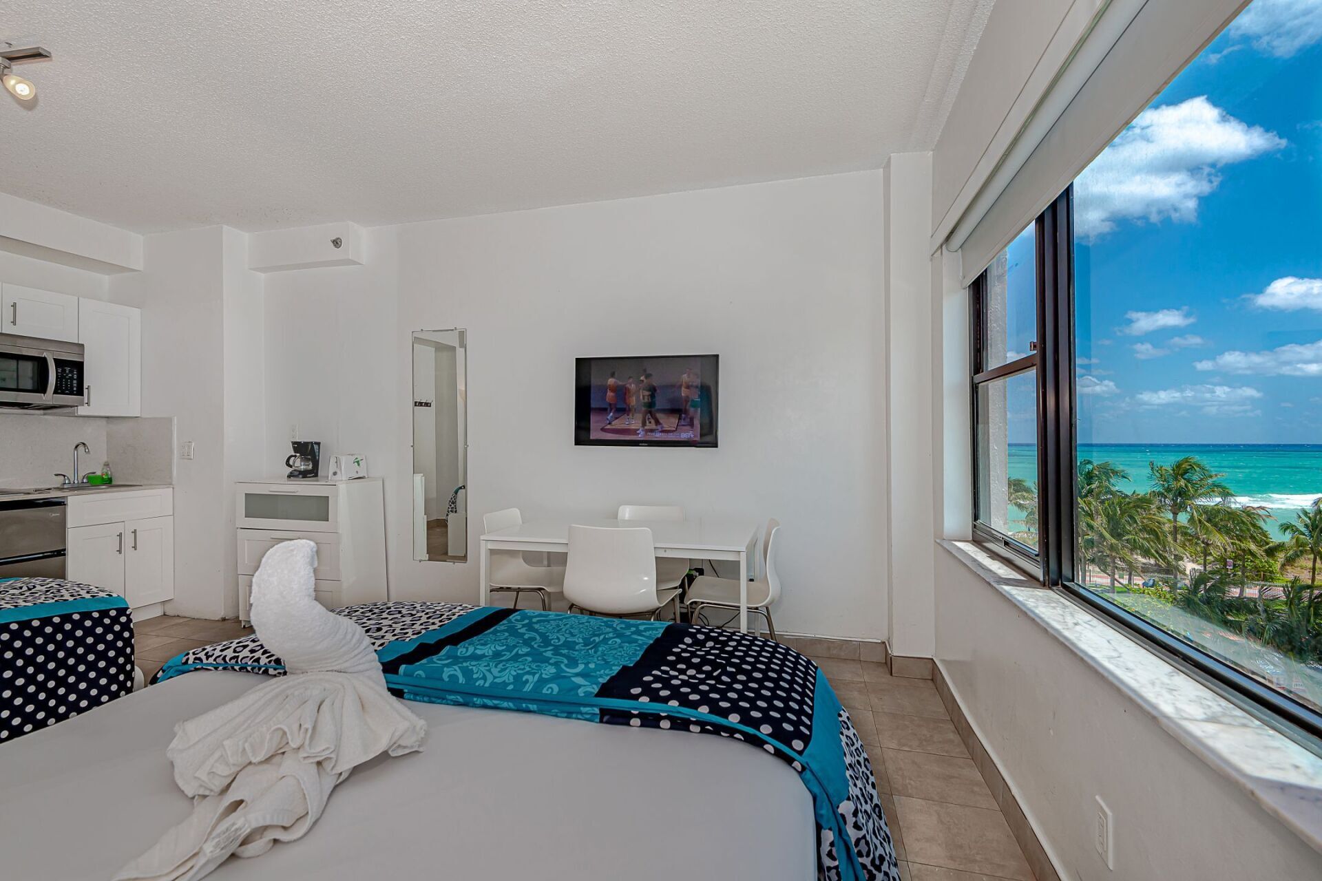 A hotel room with a bed , desk , television and a view of the ocean.