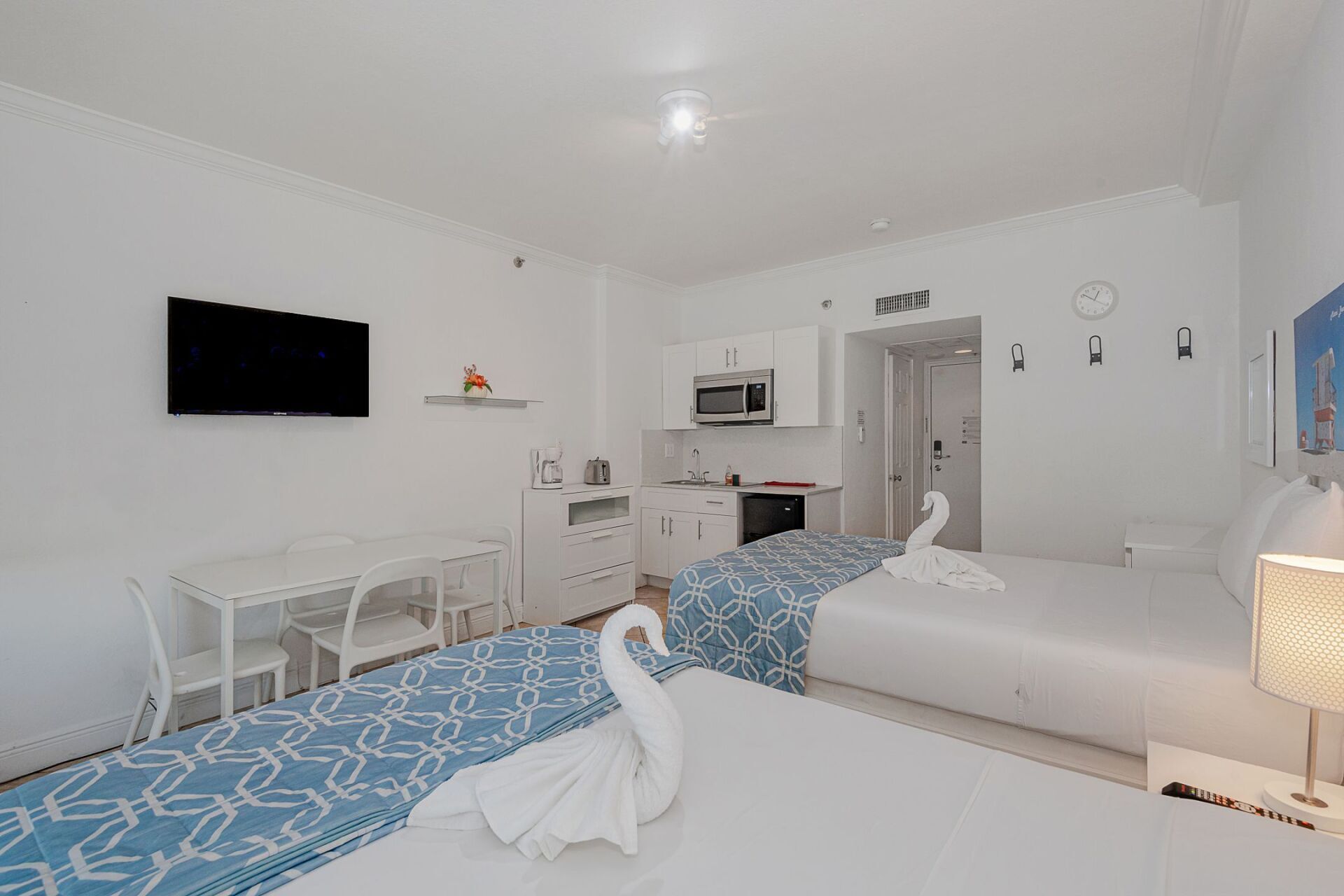 A hotel room with two beds , a desk , a television and a kitchen.