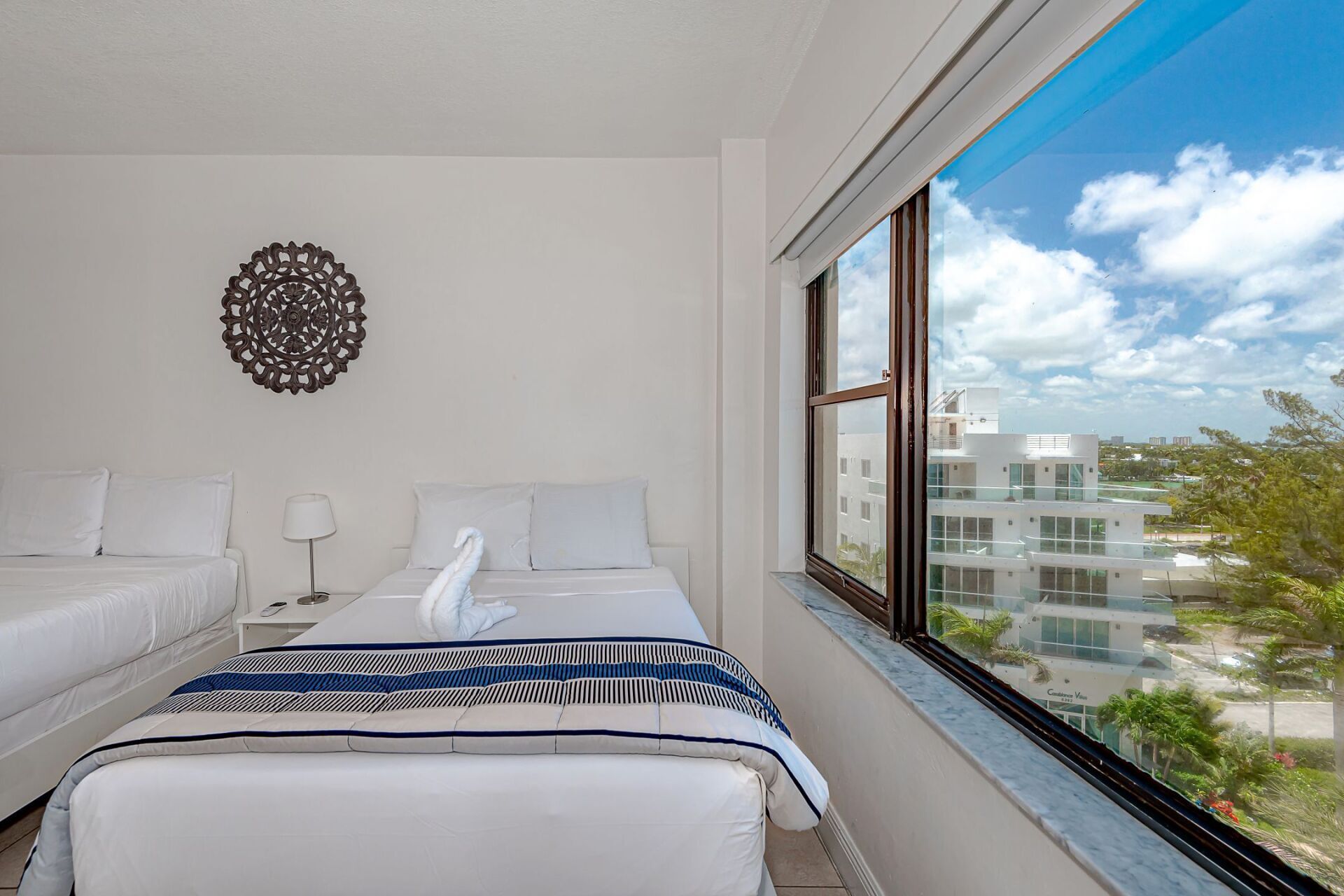A bedroom with two beds and a large window with a view of a city.