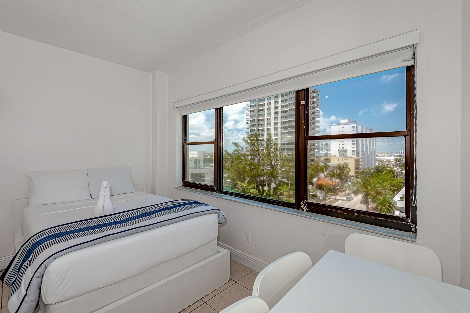 A bedroom with a bed , table and chairs and a large window.
