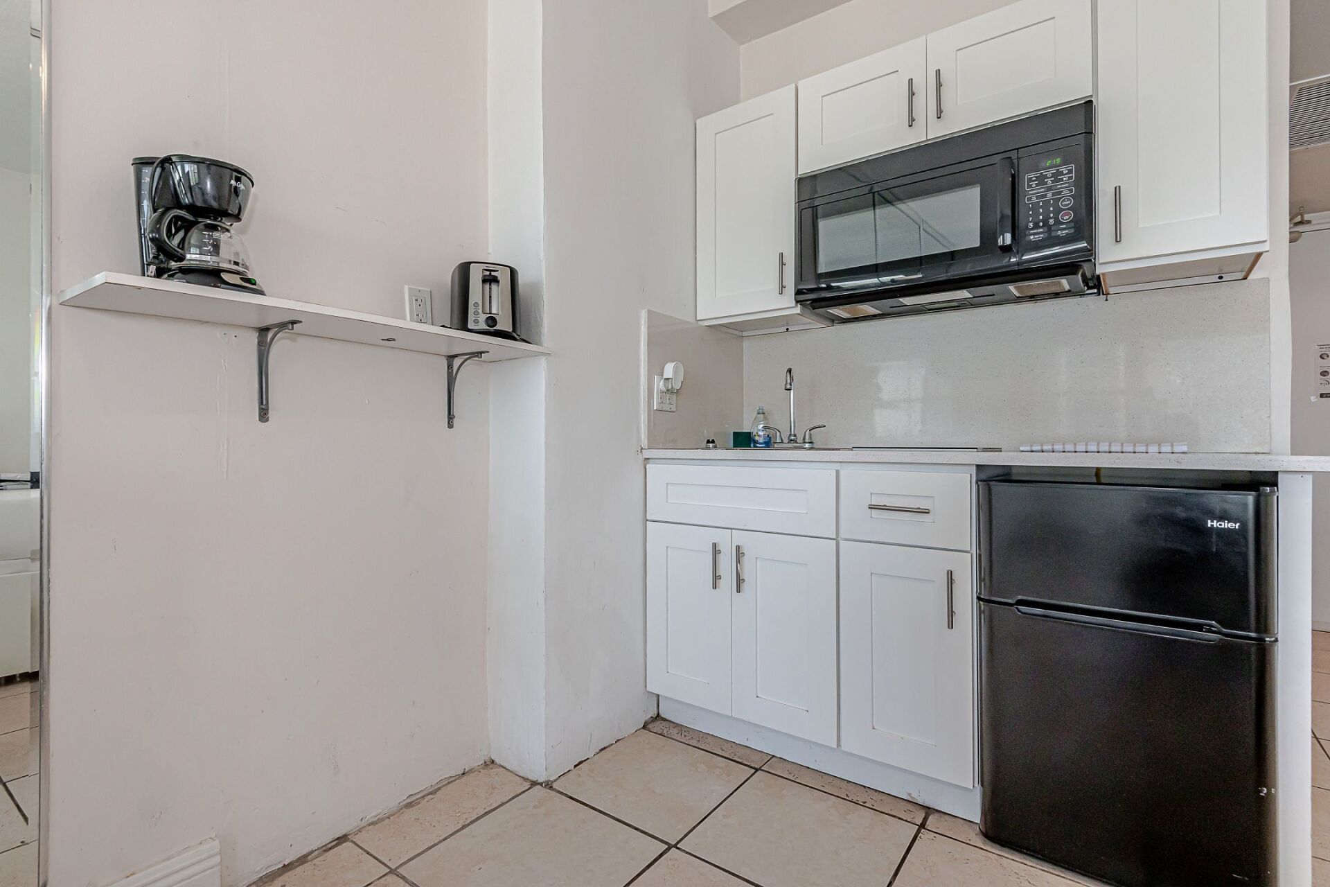 A kitchen with white cabinets , a black refrigerator , a microwave , and a coffee maker.