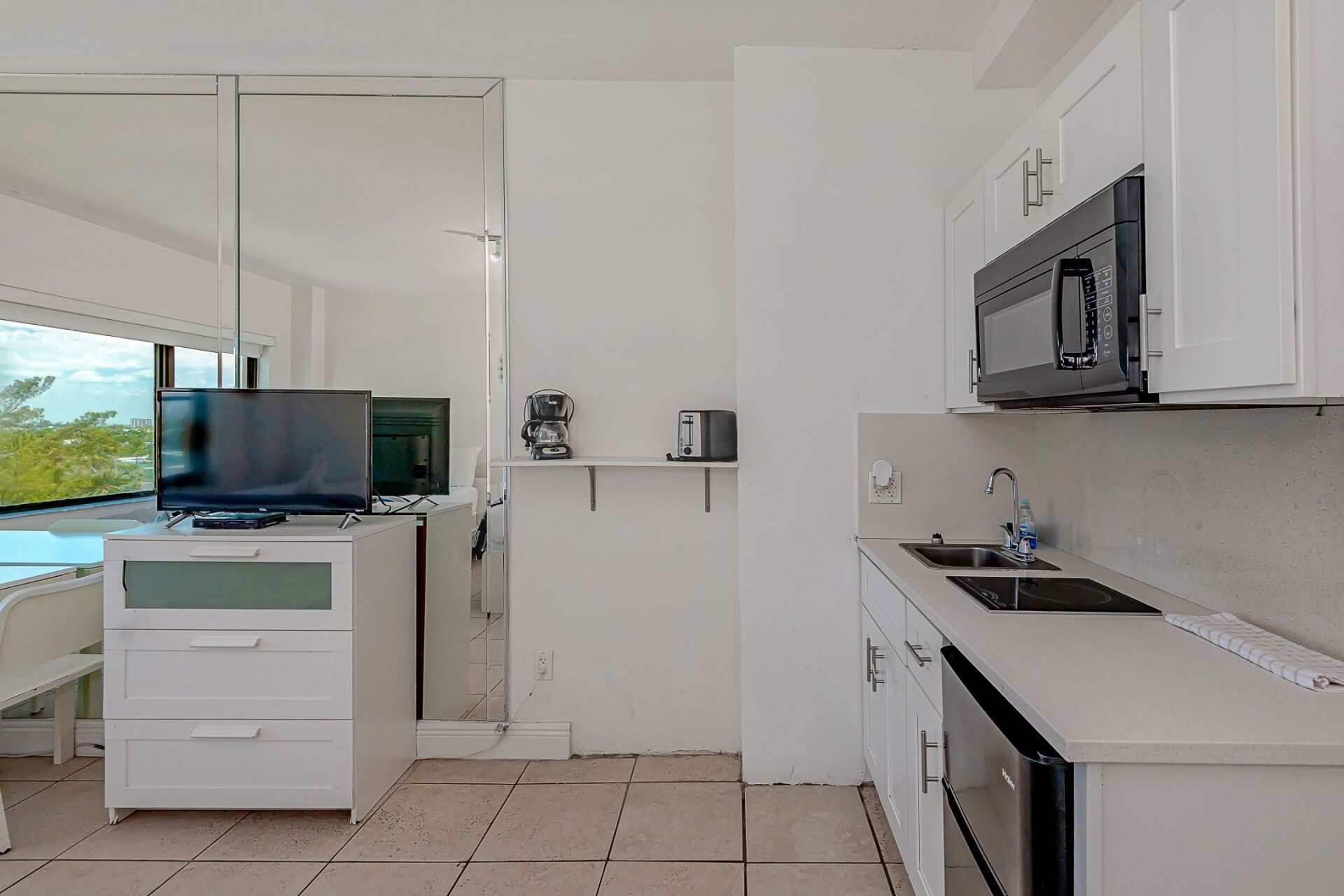 A kitchen with white cabinets and a flat screen tv