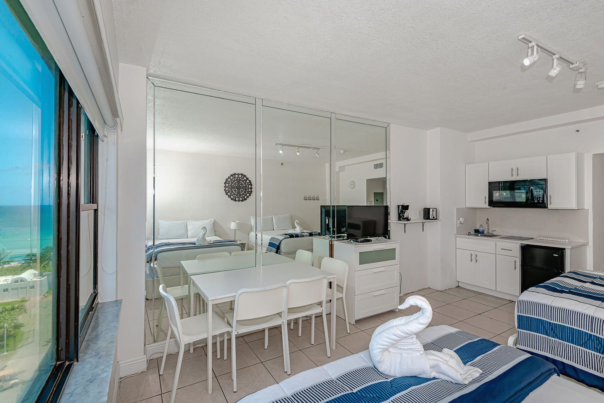 A hotel room with a table , chairs , and a swan on the bed.