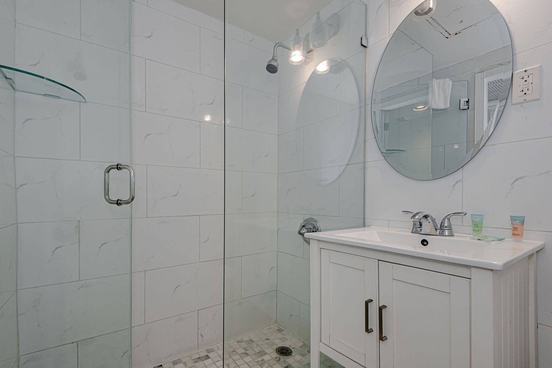 A bathroom with a sink , mirror and walk in shower.