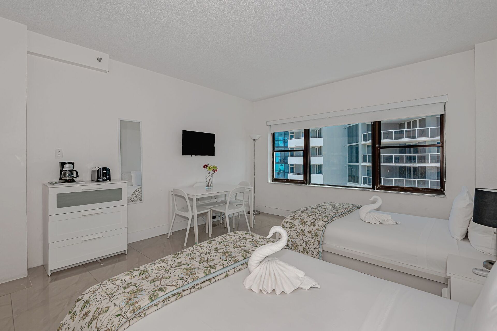 A bedroom with two beds , a dresser , a table and chairs.
