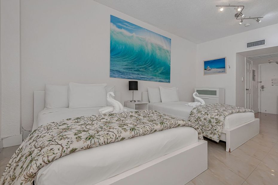 A bedroom with two beds and a picture of a wave on the wall.