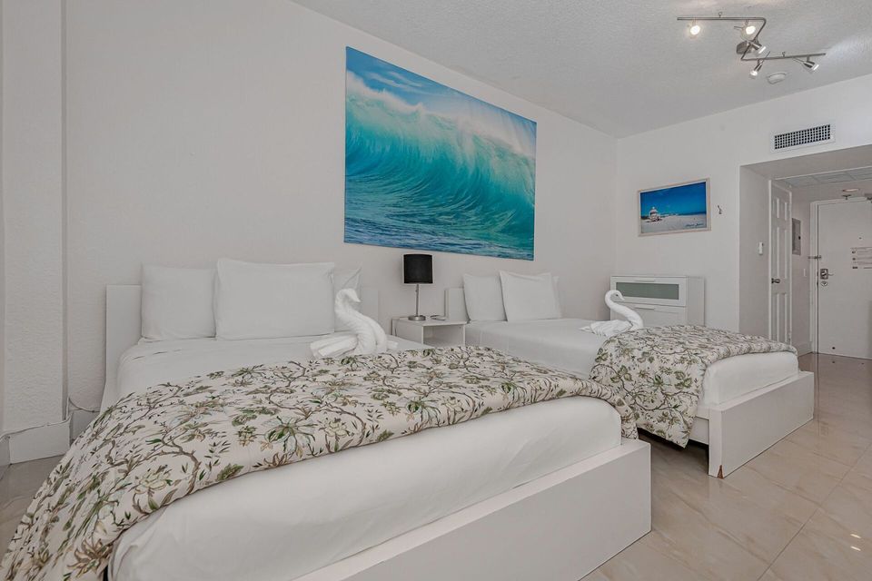 A bedroom with two beds and a picture of a wave on the wall.