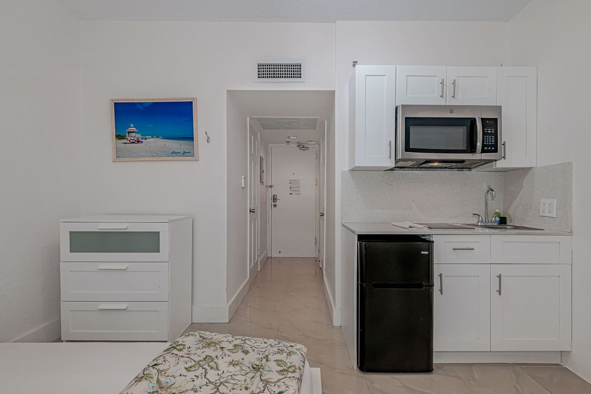 A small kitchen with a refrigerator , microwave , sink and dresser.