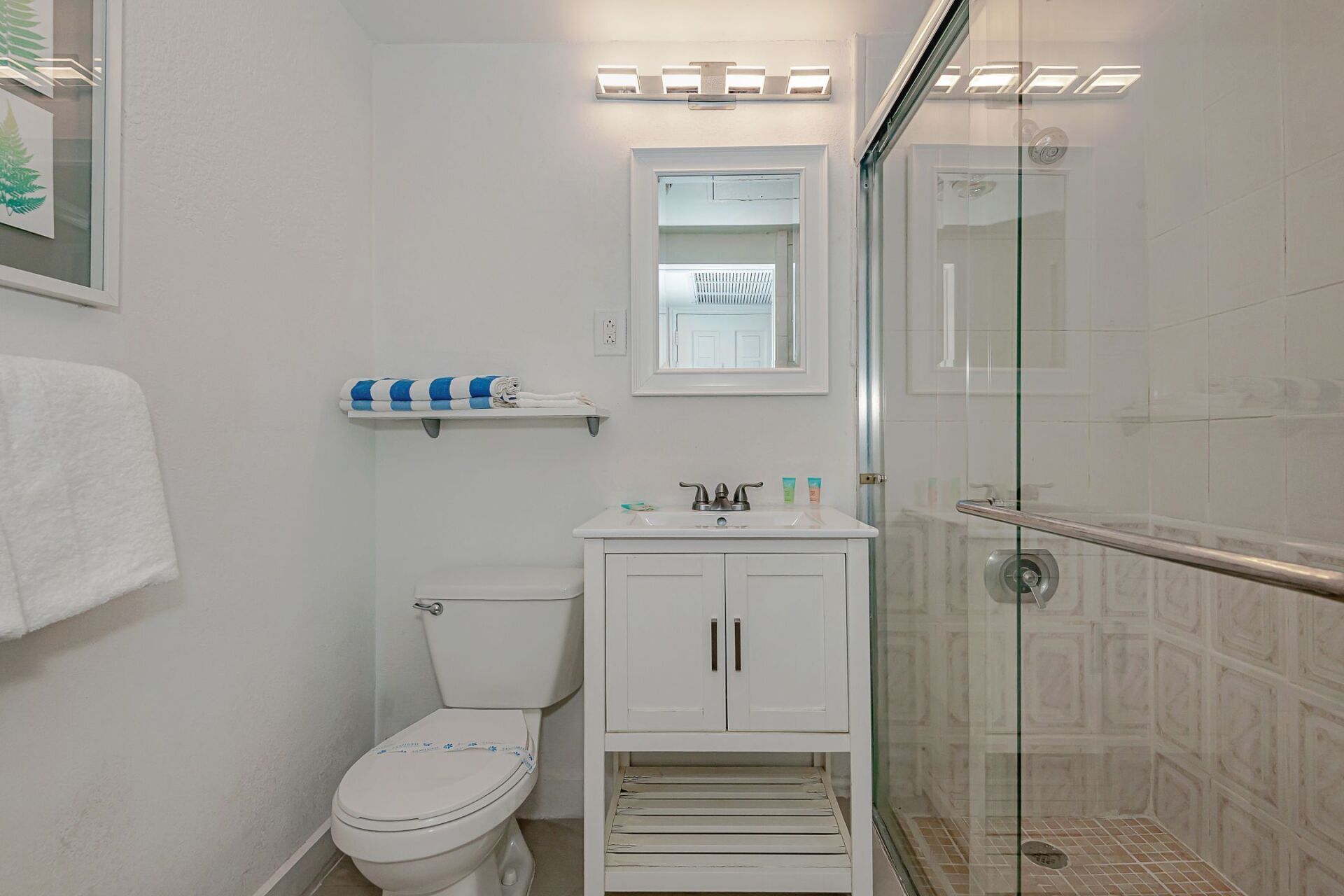 A bathroom with a toilet , sink , mirror and walk in shower.