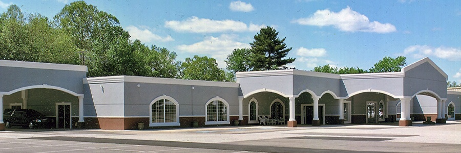 A single-story commercial building with a gray exterior, brown trim, and covered walkways; blue sky.