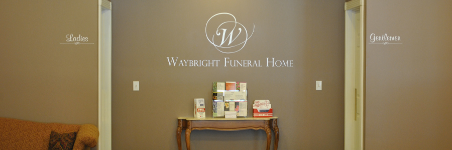 Entrance to Wright Funeral Home; brown wall with logo and table with floral arrangement and products.