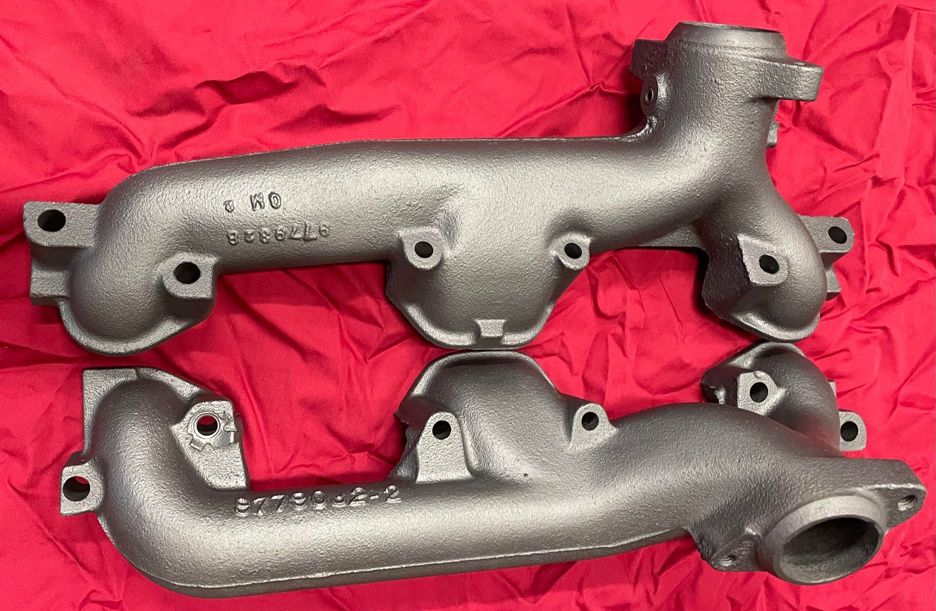 Two exhaust manifolds are sitting on top of each other on a red cloth